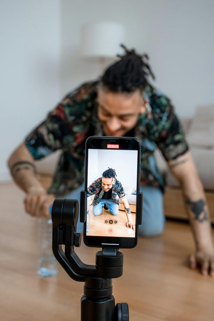 Man recording creative TikTok video at home using smartphone. Indoor setting with blurred background.